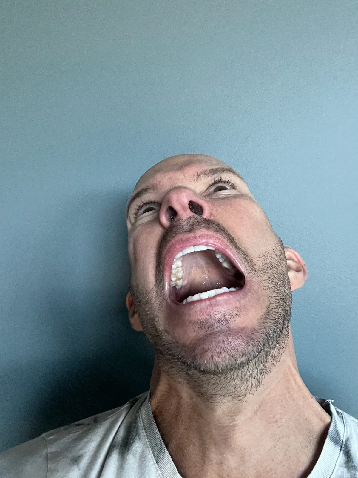 Glen looking upwards with his mouth open, photographed from below against a plain wall.